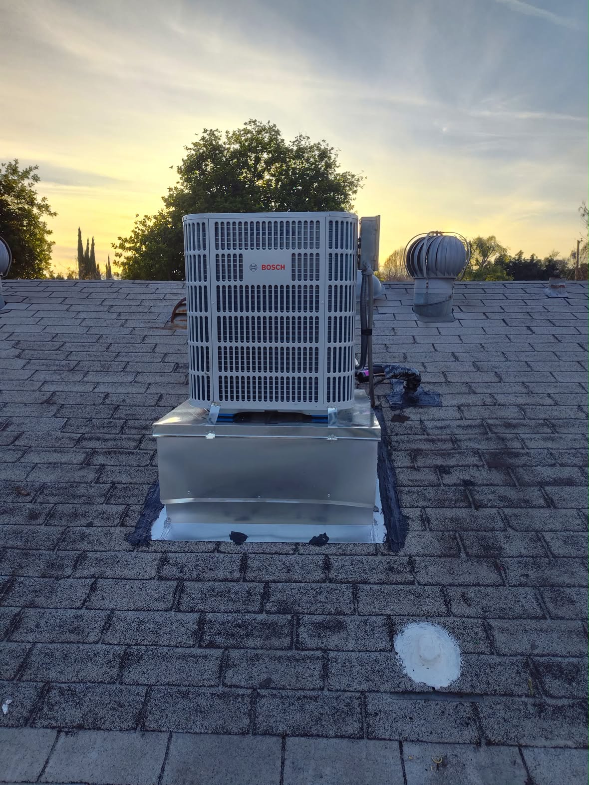 Bosch condenser set on a fabricated curb on a shingle roof at sunset